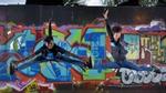 Two girls jumping in the air with their arms and legs outstretched in front of a wall covered with colourful graffiti.