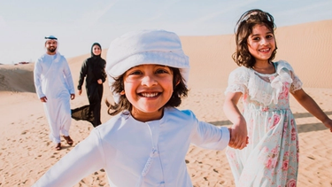 2 kids smiling holding each other's hand and parents at back looking at them