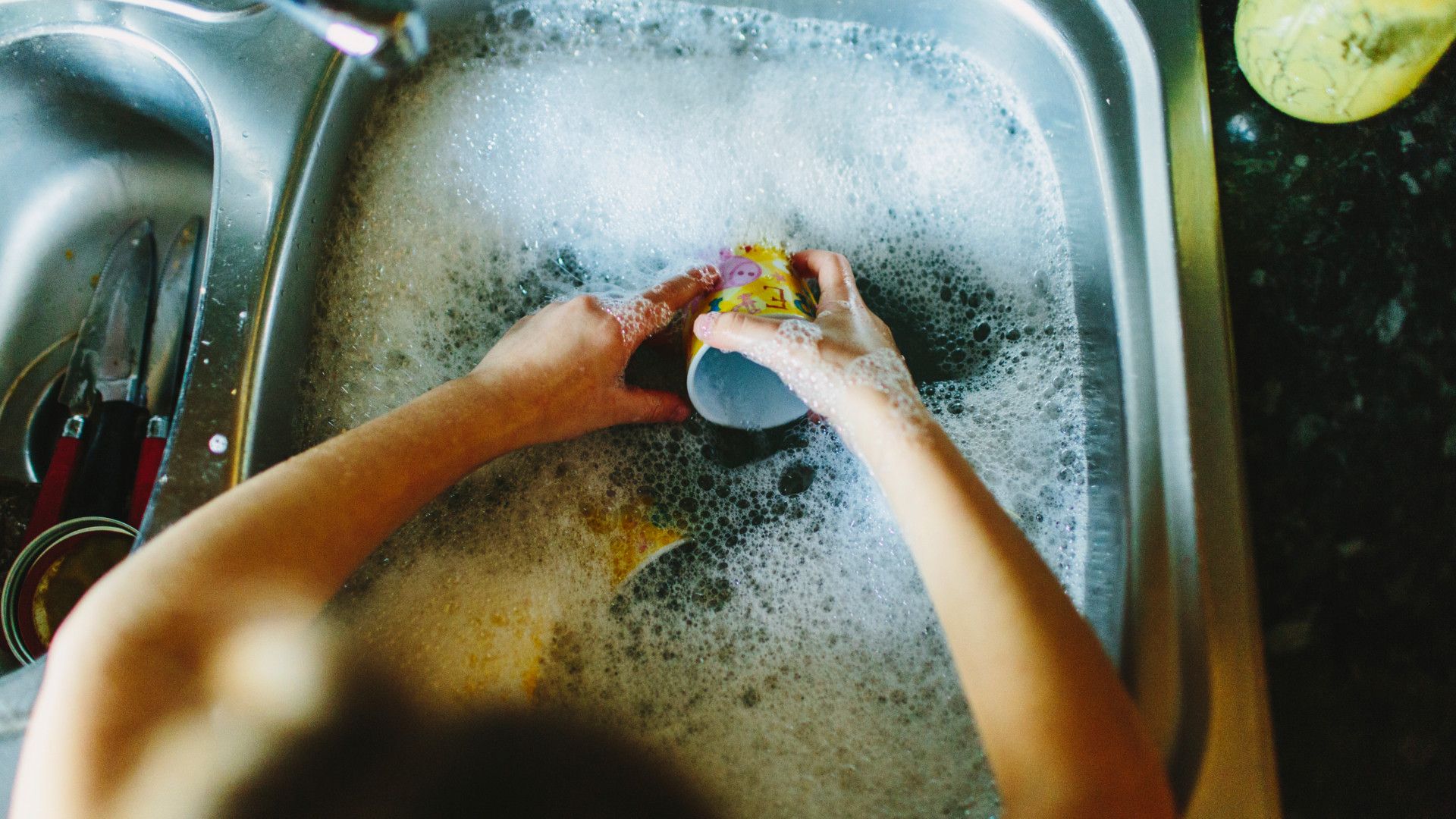 Hands in a sink washing up dirty dishes