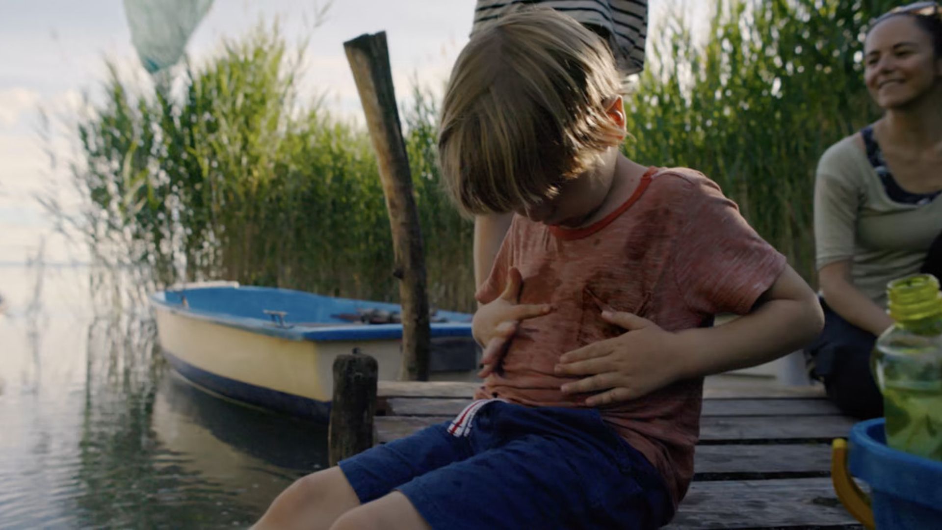 Young boy by a lake looking at dirty t-shirt 