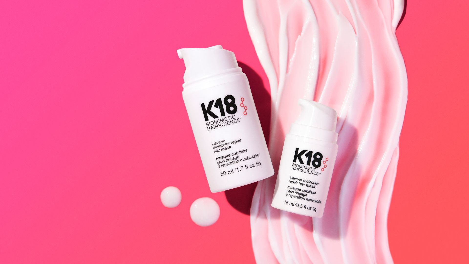 Two white bottles of K18 hair treatment placed on a pink background with swirled cream.