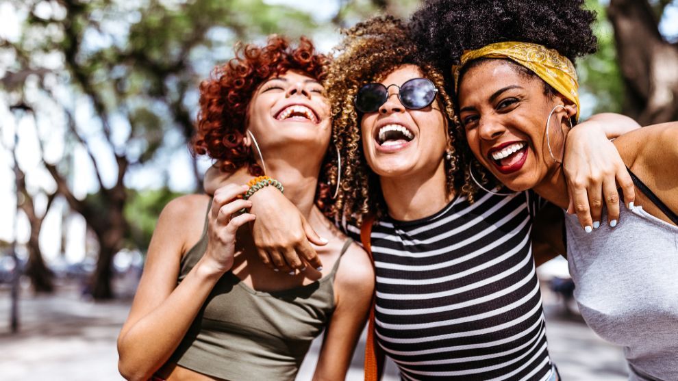 A photograph of three women with their arms around each other's shoulders. 